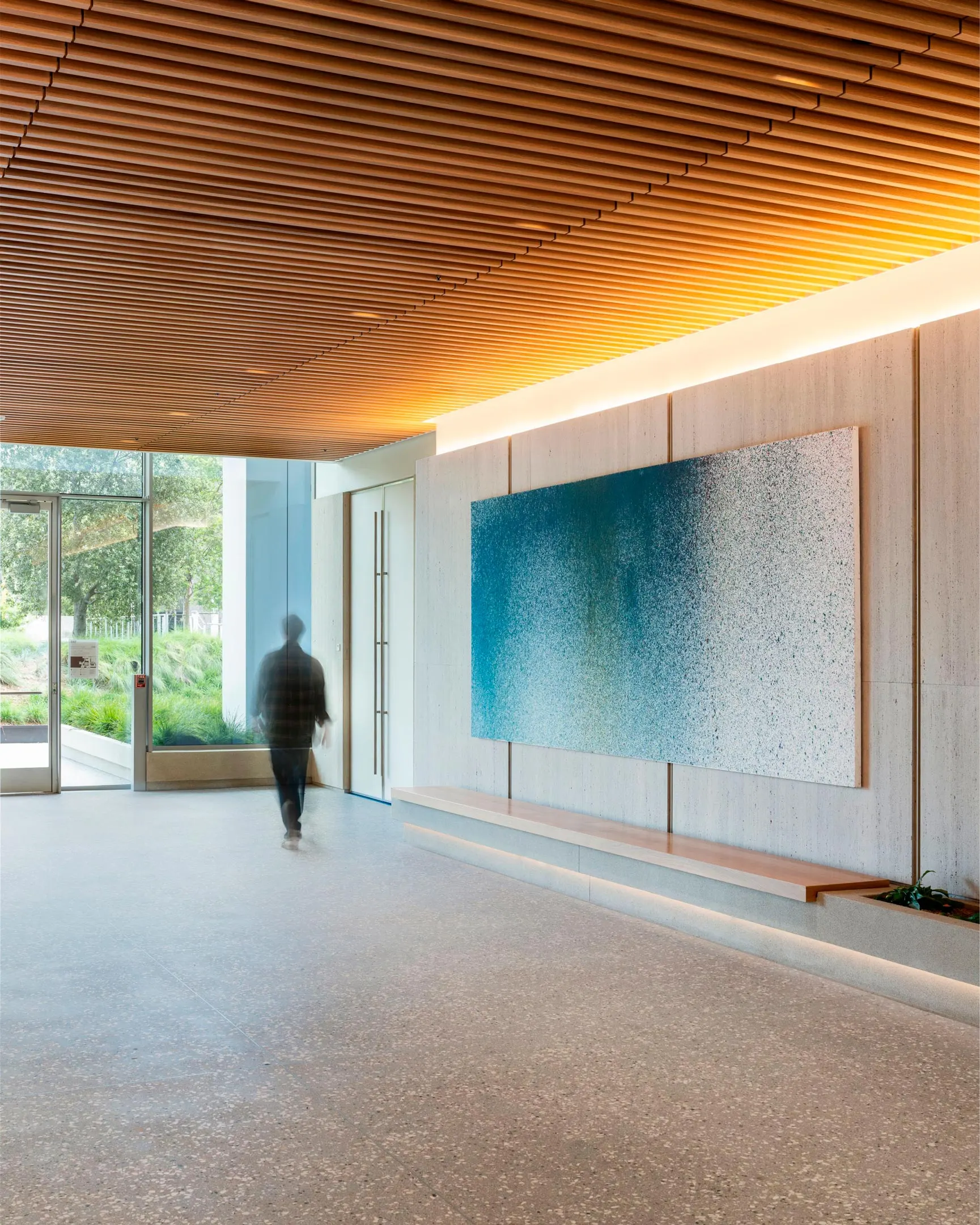 Building lobby with a wood slat ceiling and a large blue and white speckled painting above a bench
