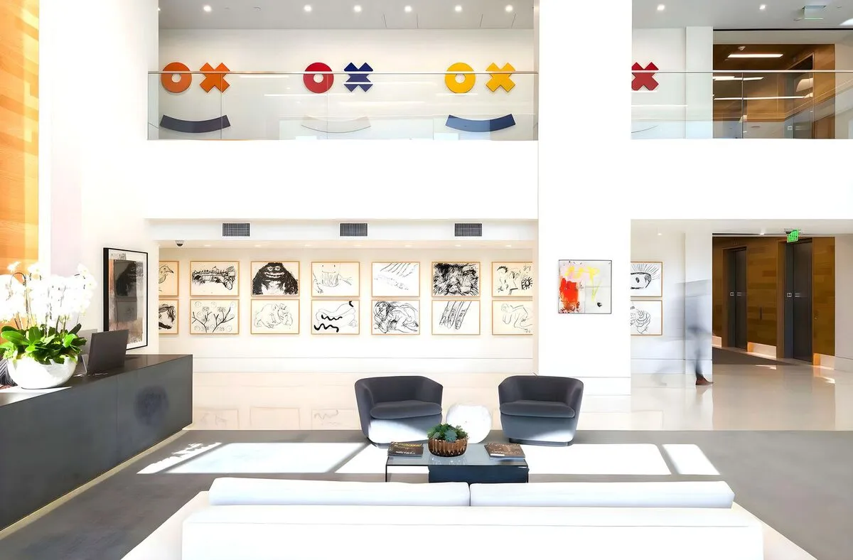 Two-story office lobby with a gallery wall of framed black and white drawings and colorful wall graphics above