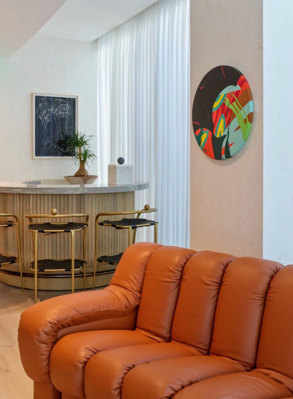 Round abstract painting in red, green and teal on a wall beside a lounge bar with brass stools