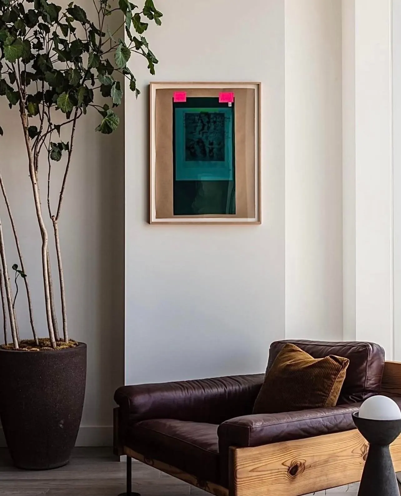 Framed teal and black work on paper with pink tabs above a brown leather sofa