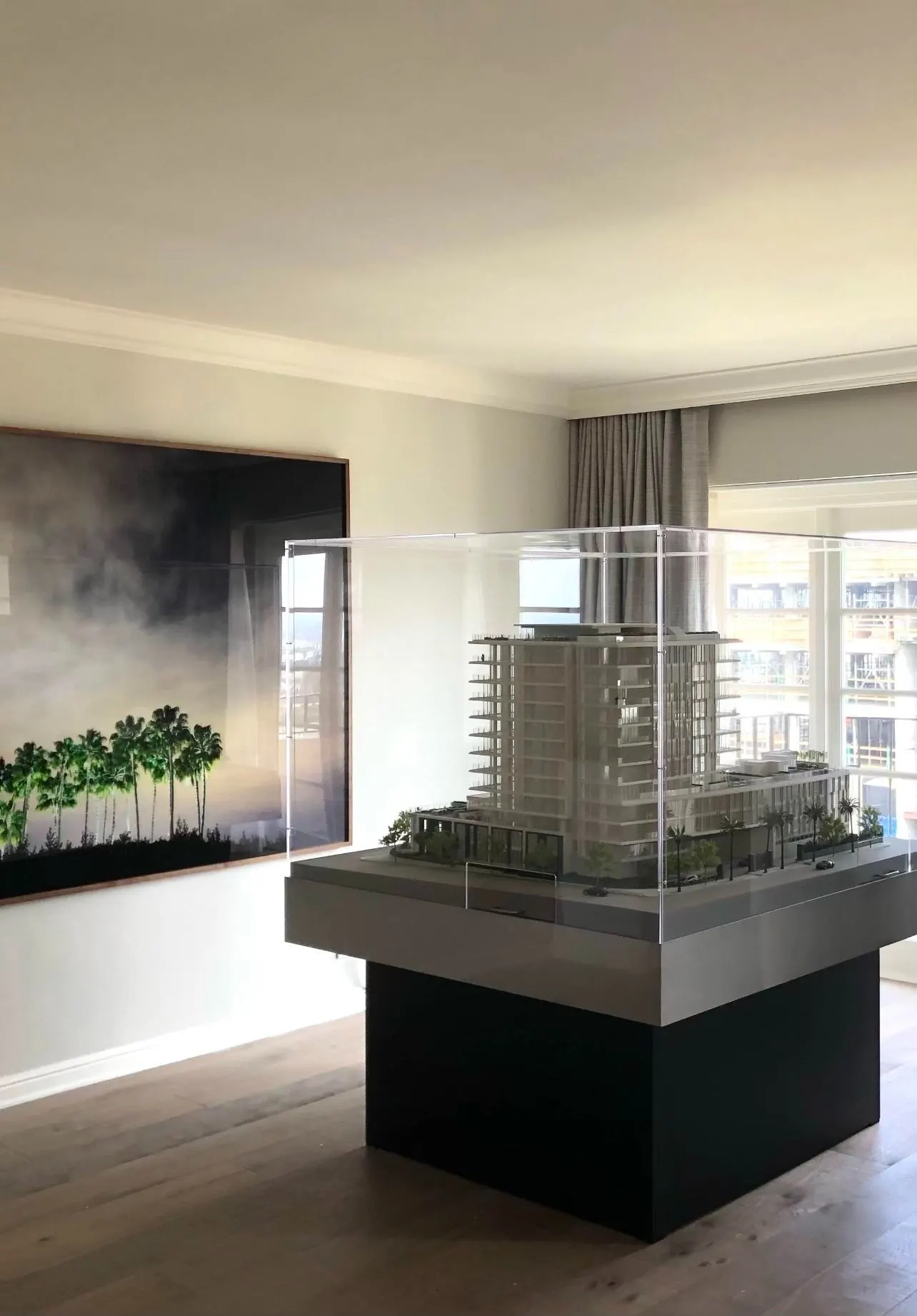 Large dark photograph of palm trees in mist beside an architectural model of the Four Seasons Residences tower