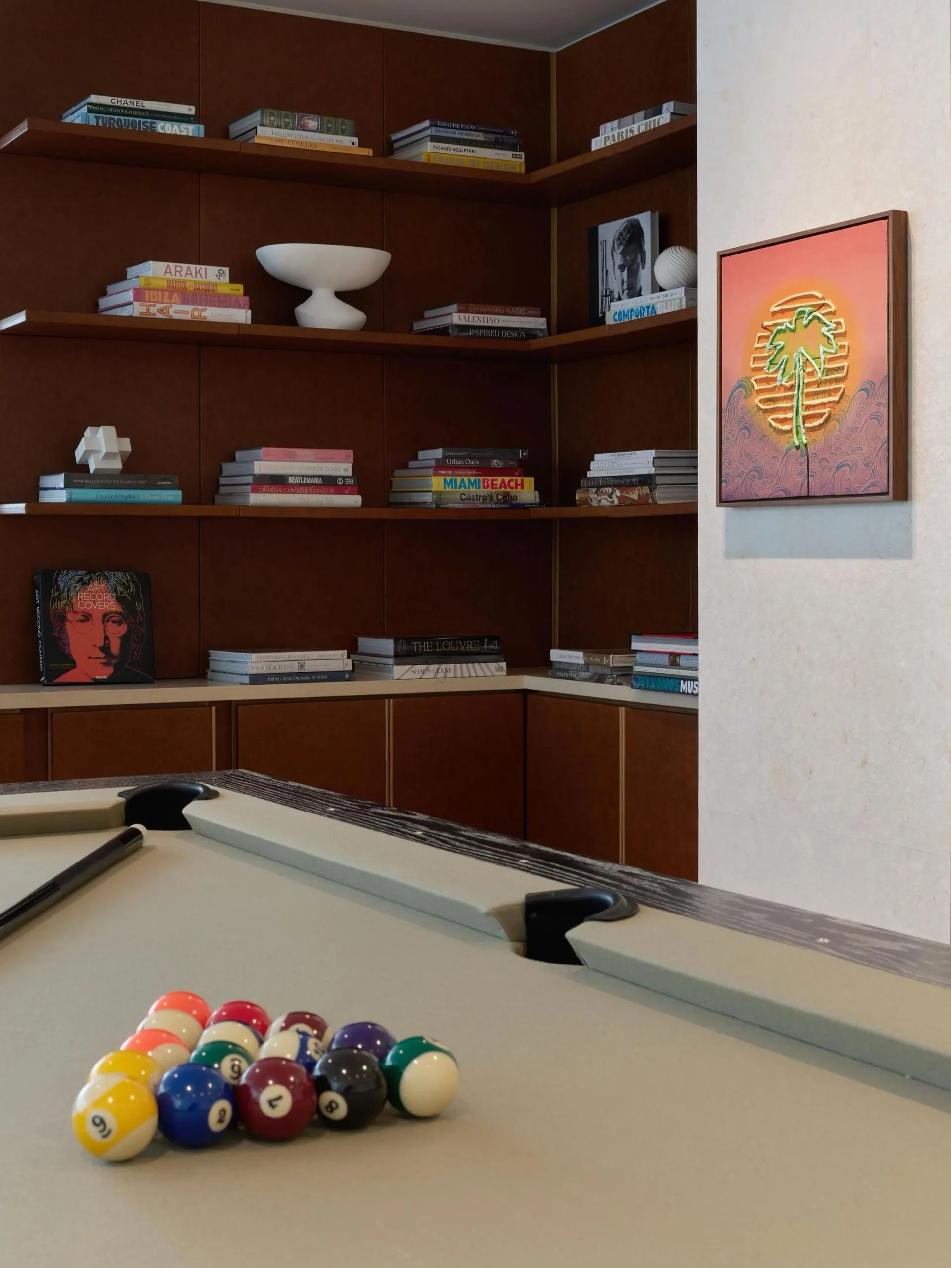 Game room with a pool table, wood bookshelves and a framed neon palm tree artwork on an orange background