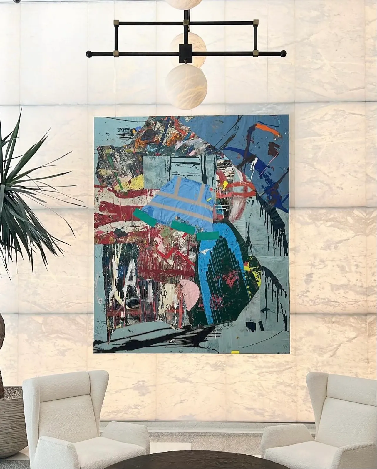 Lobby with a large blue collaged abstract painting on a backlit onyx wall between two white armchairs