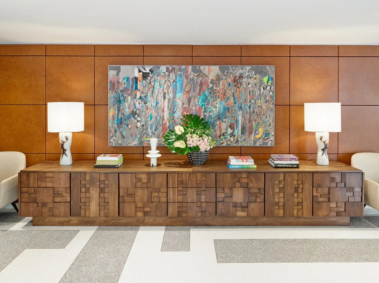 Large colorful abstract painting above a carved wood credenza flanked by white lamps in a residential lobby