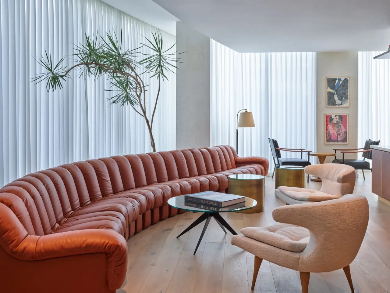 Residents' lounge with a long curved rust leather sofa and two framed portrait paintings near tall curtains