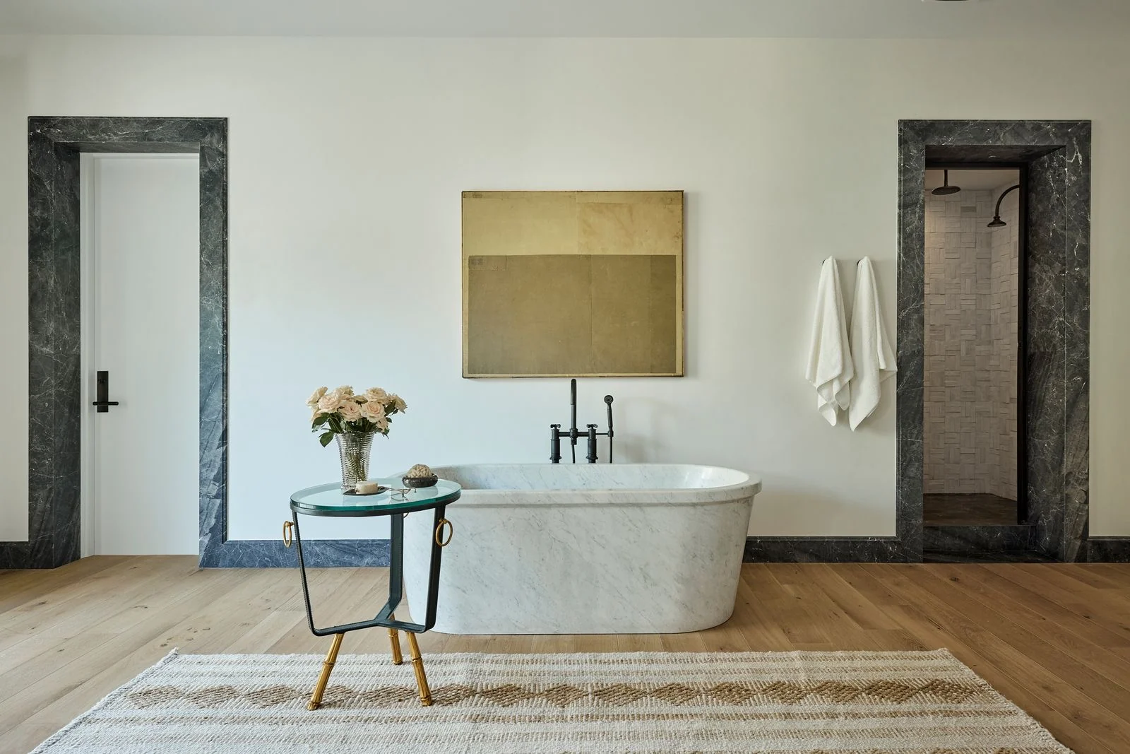 Marble freestanding bathtub beneath a gold and olive abstract painting in a bright bathroom