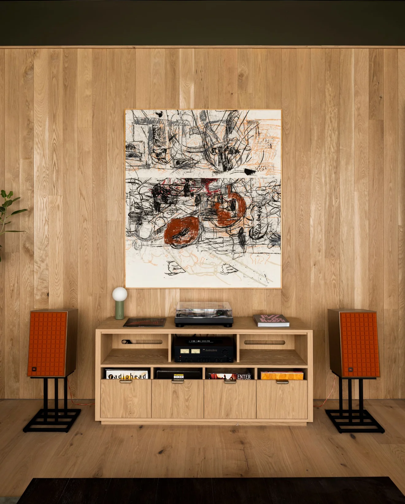 Black and orange abstract drawing on a wood-paneled wall above a record console between orange speakers