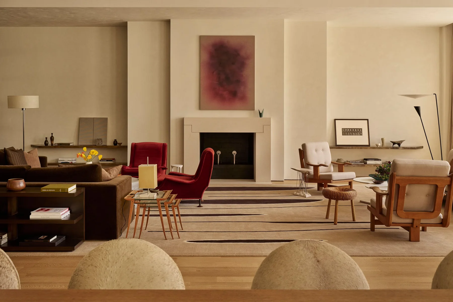 Living room with a deep red abstract painting above a stone fireplace and red velvet armchairs