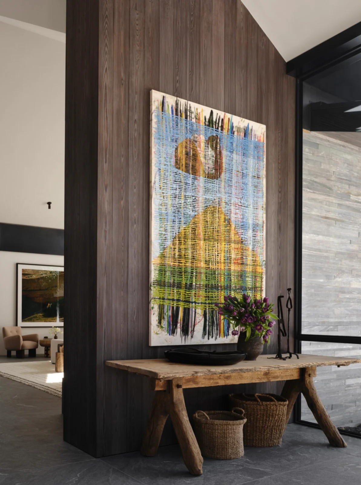 Large blue and yellow painting of layered lines on a dark wood wall above a rustic console table