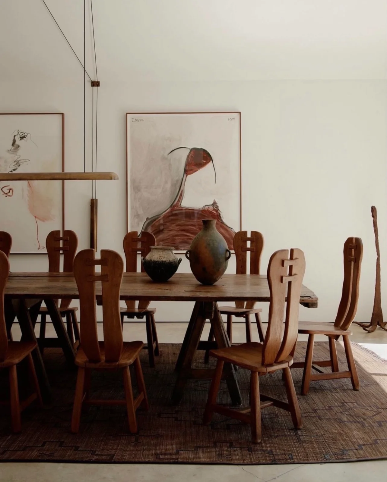 Two framed abstract drawings in red and black above a long wooden dining table with carved chairs