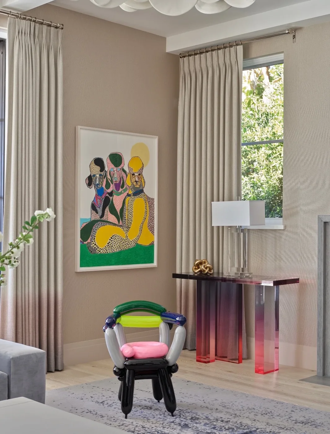 Colorful painting of three seated dogs above a pink acrylic console and a balloon-shaped chair in a Palm Beach home