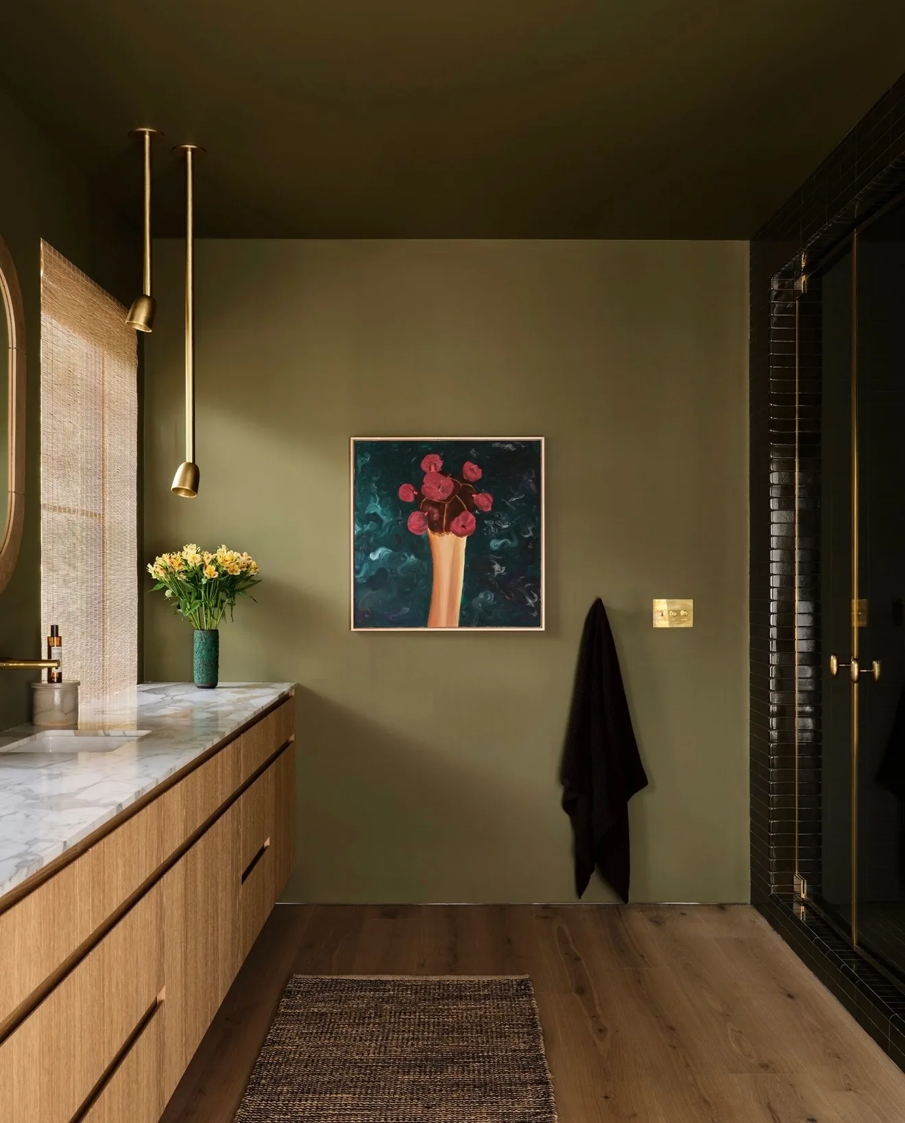 Olive green bathroom with a dark painting of red flowers in a vase above a hanging towel