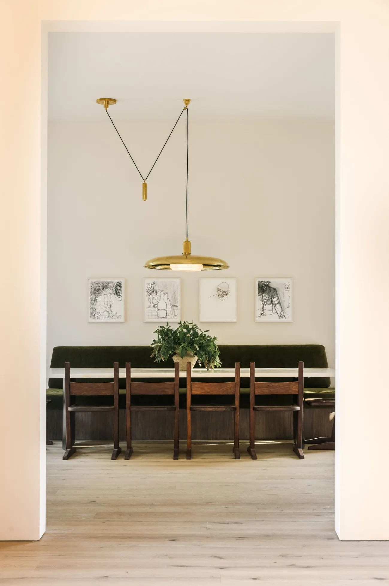 Four framed black and white figure drawings above a green banquette and long dining table, seen through a doorway