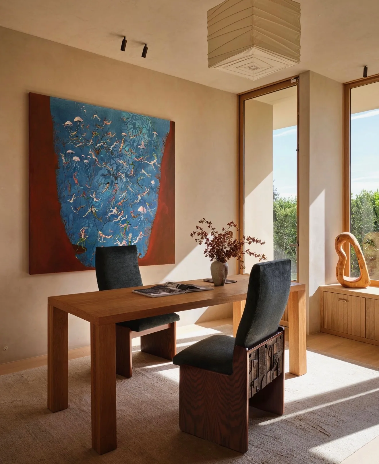 Large blue and red painting of floating figures behind a wooden desk in a sunlit home office