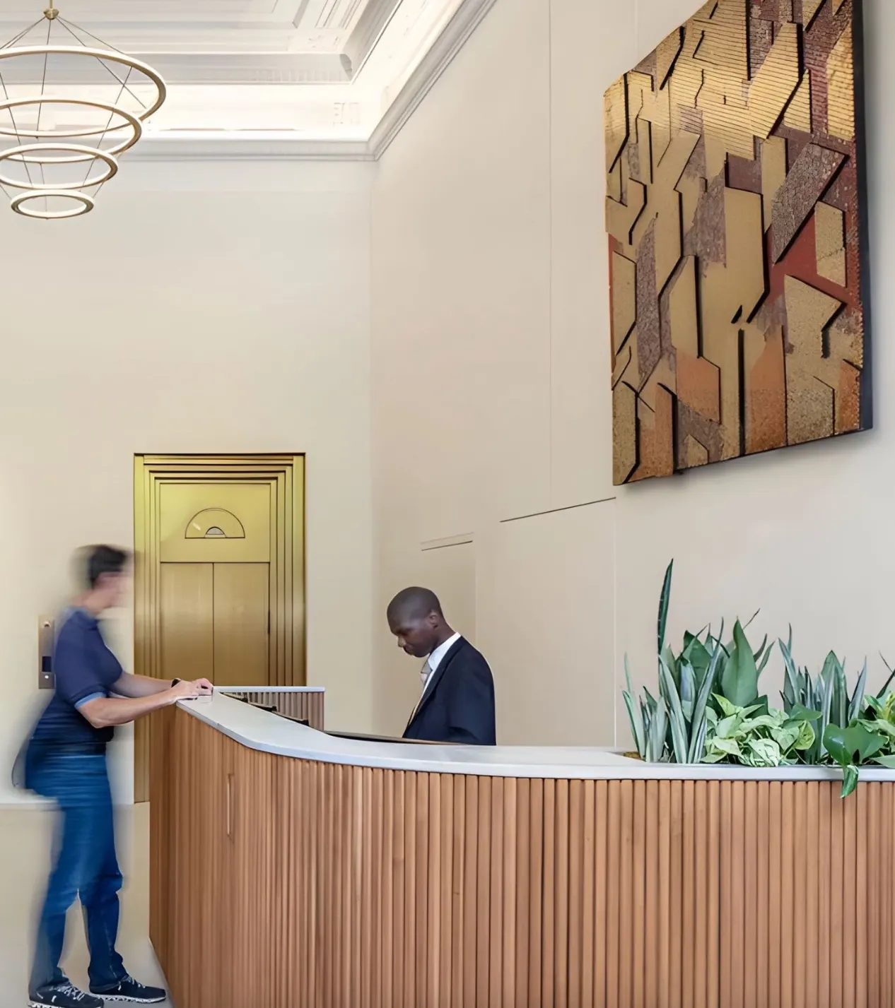 Building lobby with a wood-slatted reception desk and a large gold and copper geometric wall relief