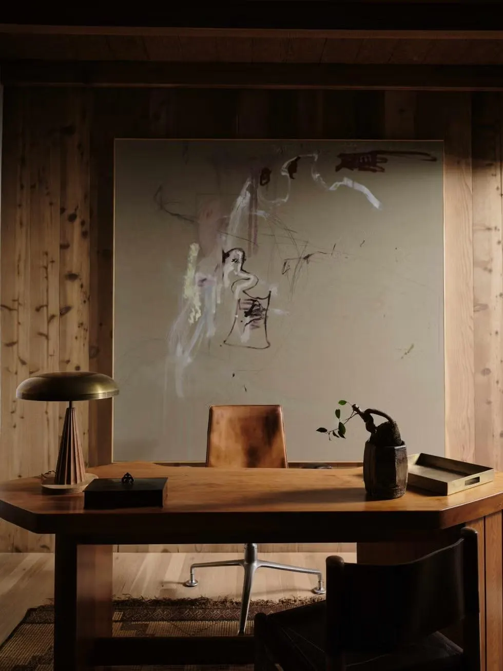 Wood-paneled study with a brass lamp on a desk and a large pale gestural painting behind