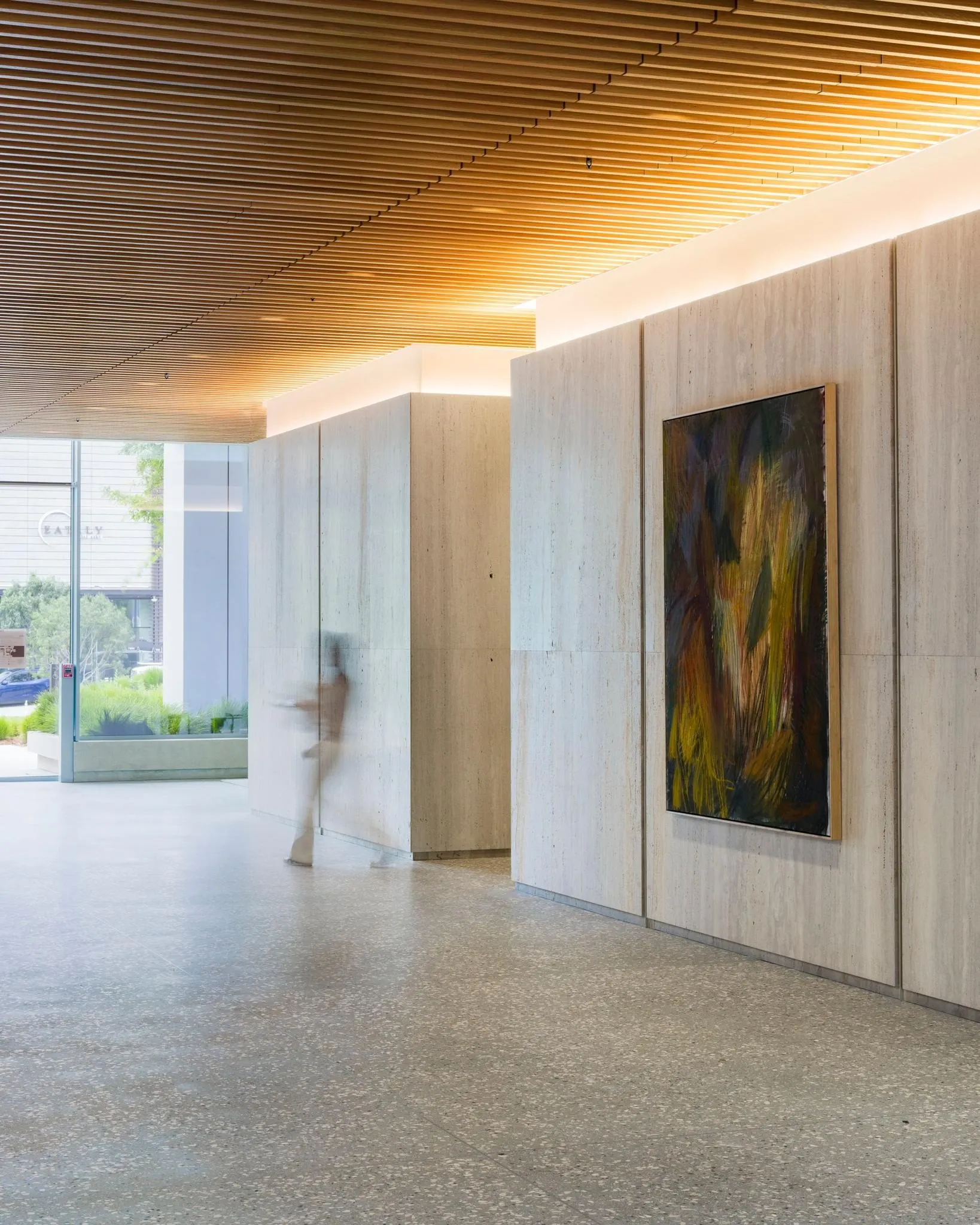 Dark painting with yellow and green brushstrokes on a travertine wall under a wood slat ceiling, artwork by Gene A'Hern