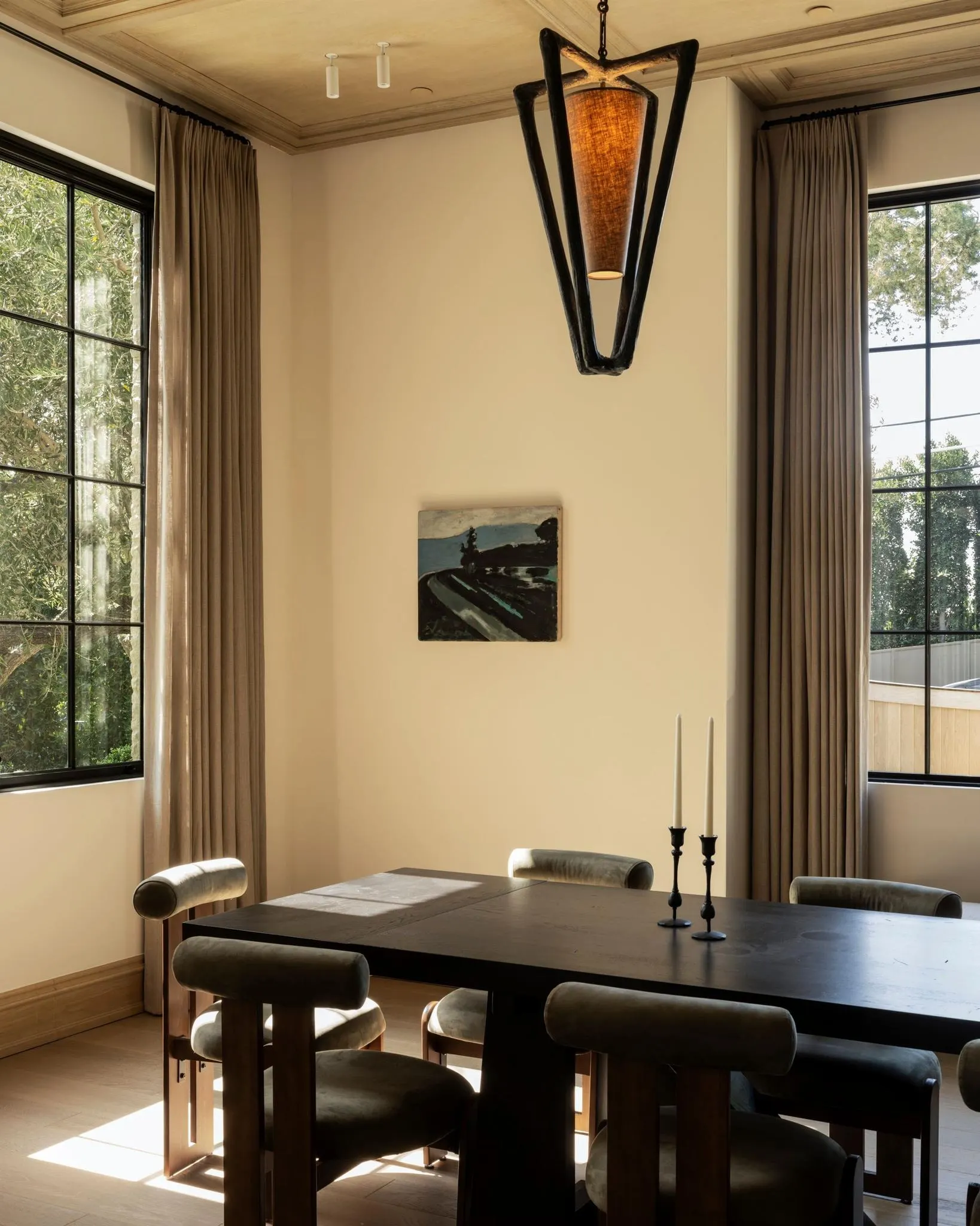 Small dark landscape painting on a cream wall above a black dining table with upholstered chairs, artwork by Aaron Wrinkle