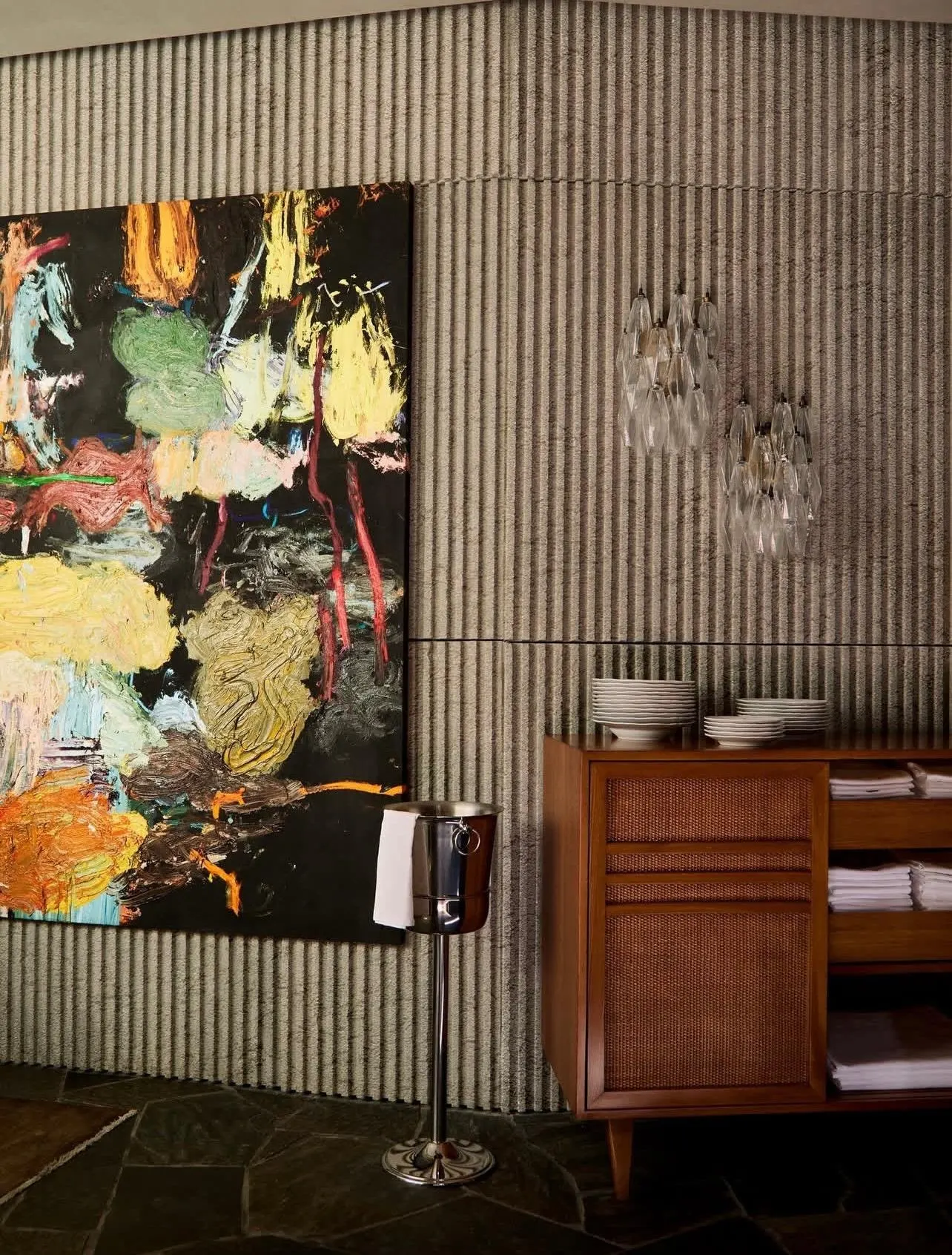 Large thickly painted abstract canvas in yellow, green and orange beside a wood sideboard on a ribbed wall