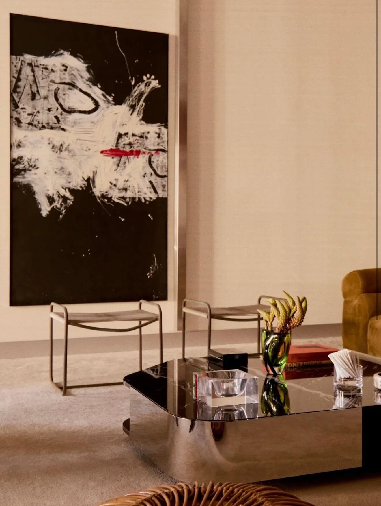 Black canvas with white and red gestural marks behind leather stools and a mirrored coffee table