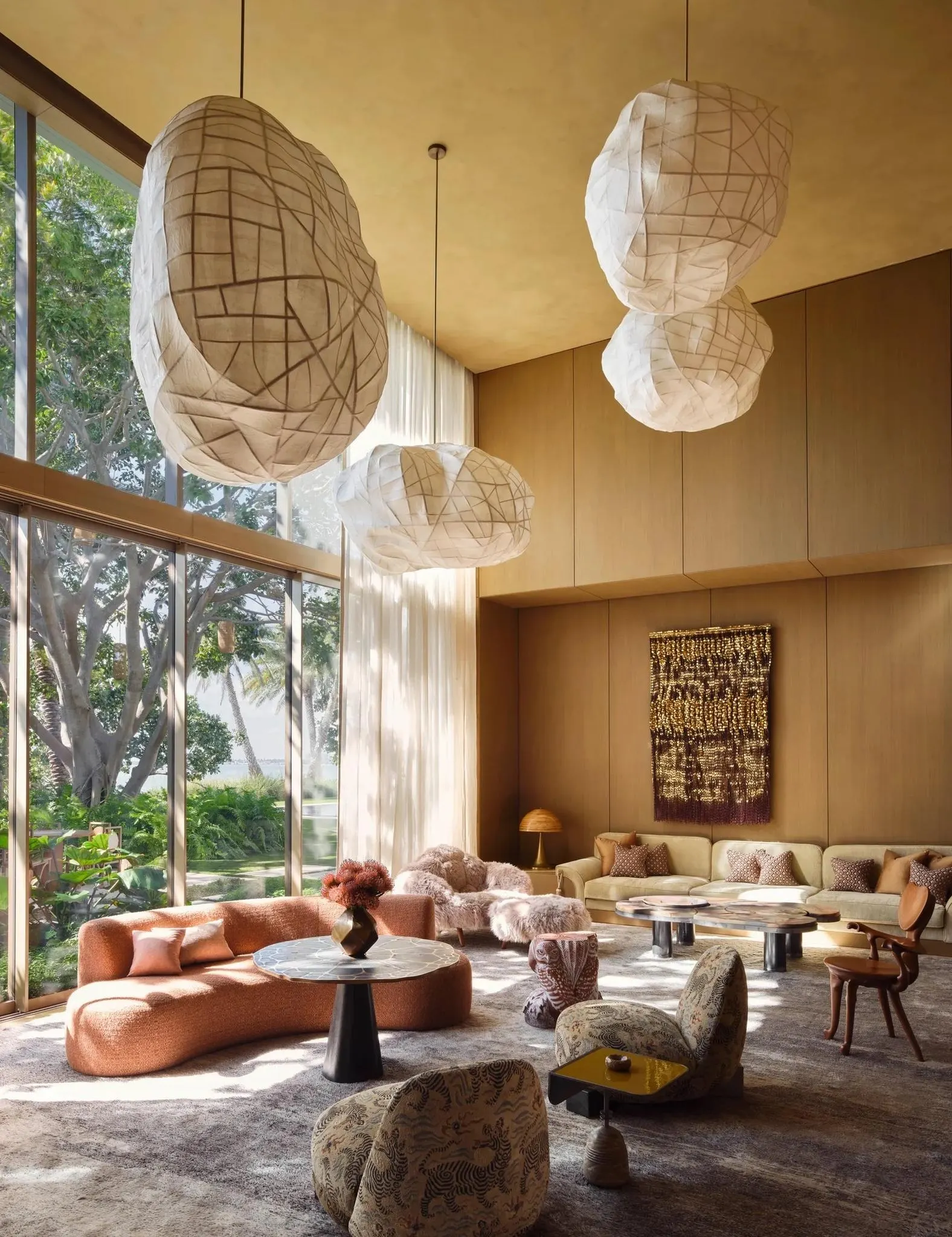 Double height living room with large paper pendant lights, a curved pink sofa and a woven wall hanging
