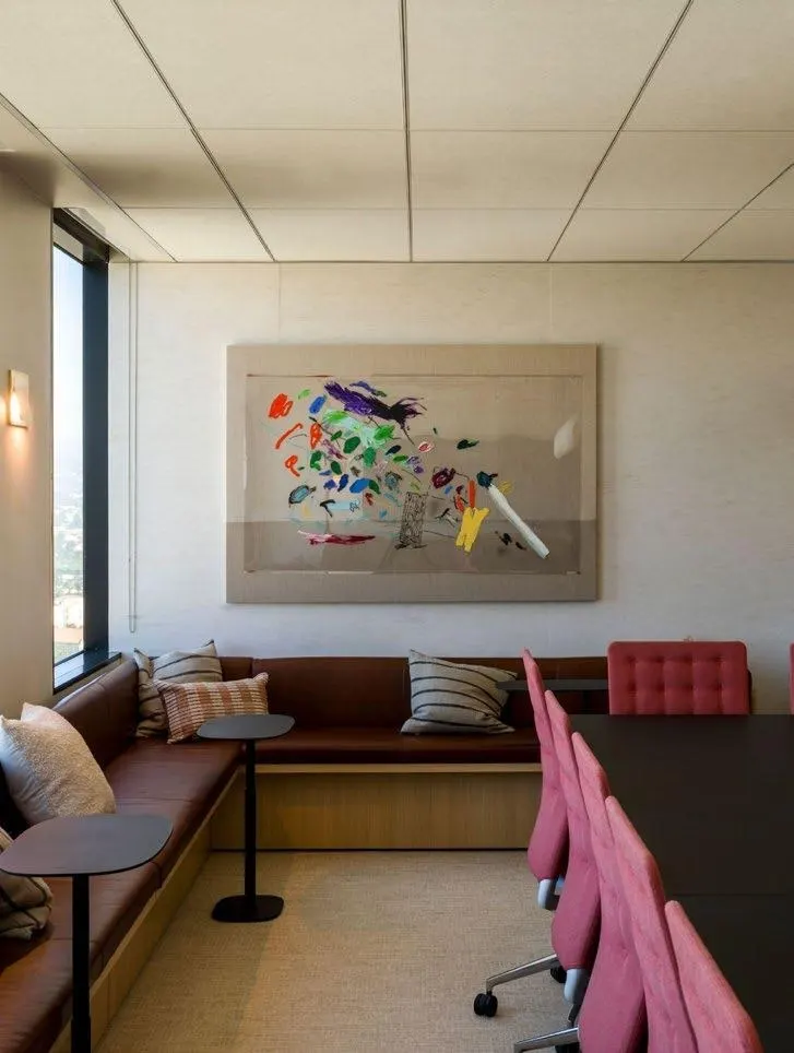 Meeting room with a leather banquette, pink chairs and a large colorful gestural painting on raw canvas