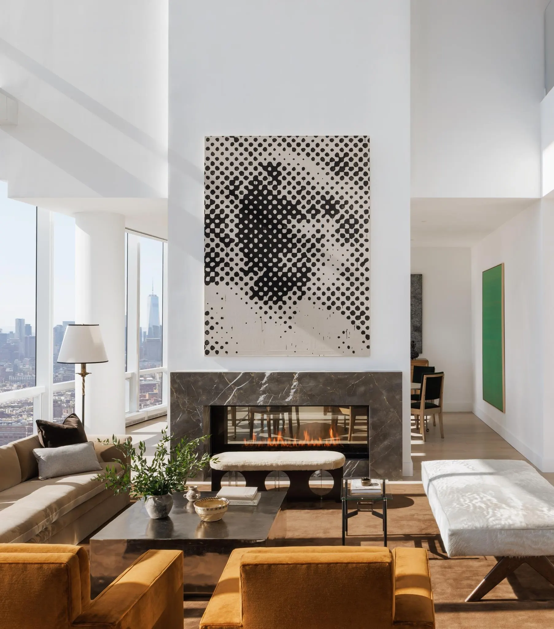Double-height living room with a large halftone artwork above a dark marble fireplace and city views
