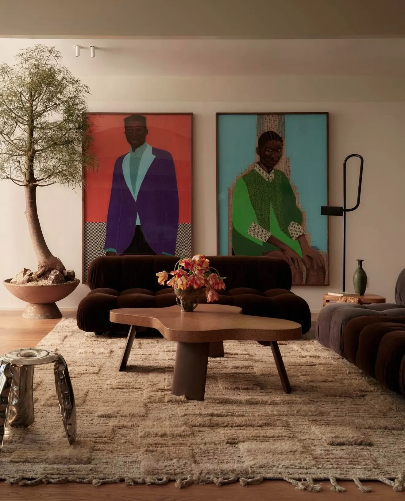 Living room with two large portrait paintings of seated figures above a dark velvet sofa and sculptural coffee table