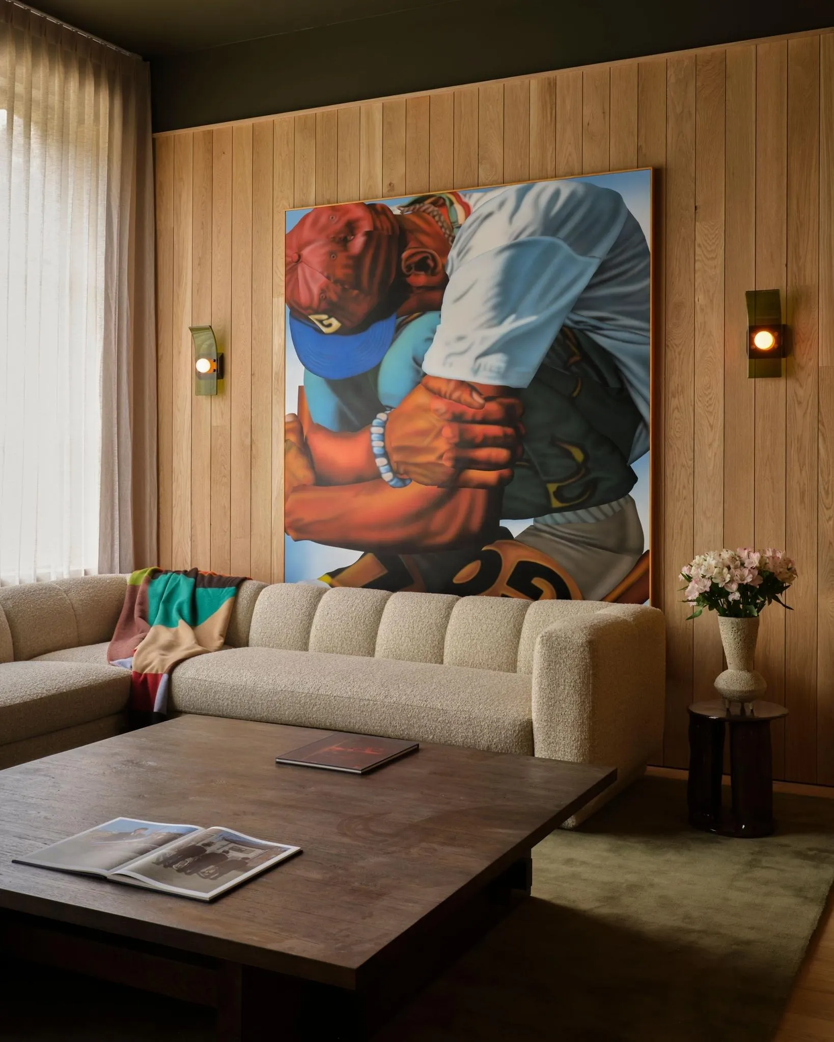 Large painting of two baseball players embracing above a cream sofa on a wood paneled wall, artwork by Alic Brock