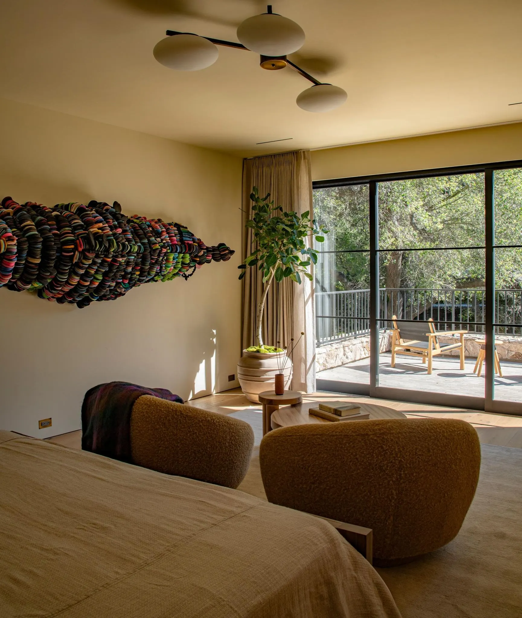 Long multicolored textile wall sculpture above a bed in a bedroom opening onto a terrace, artwork by Takunda Regis Billiatm