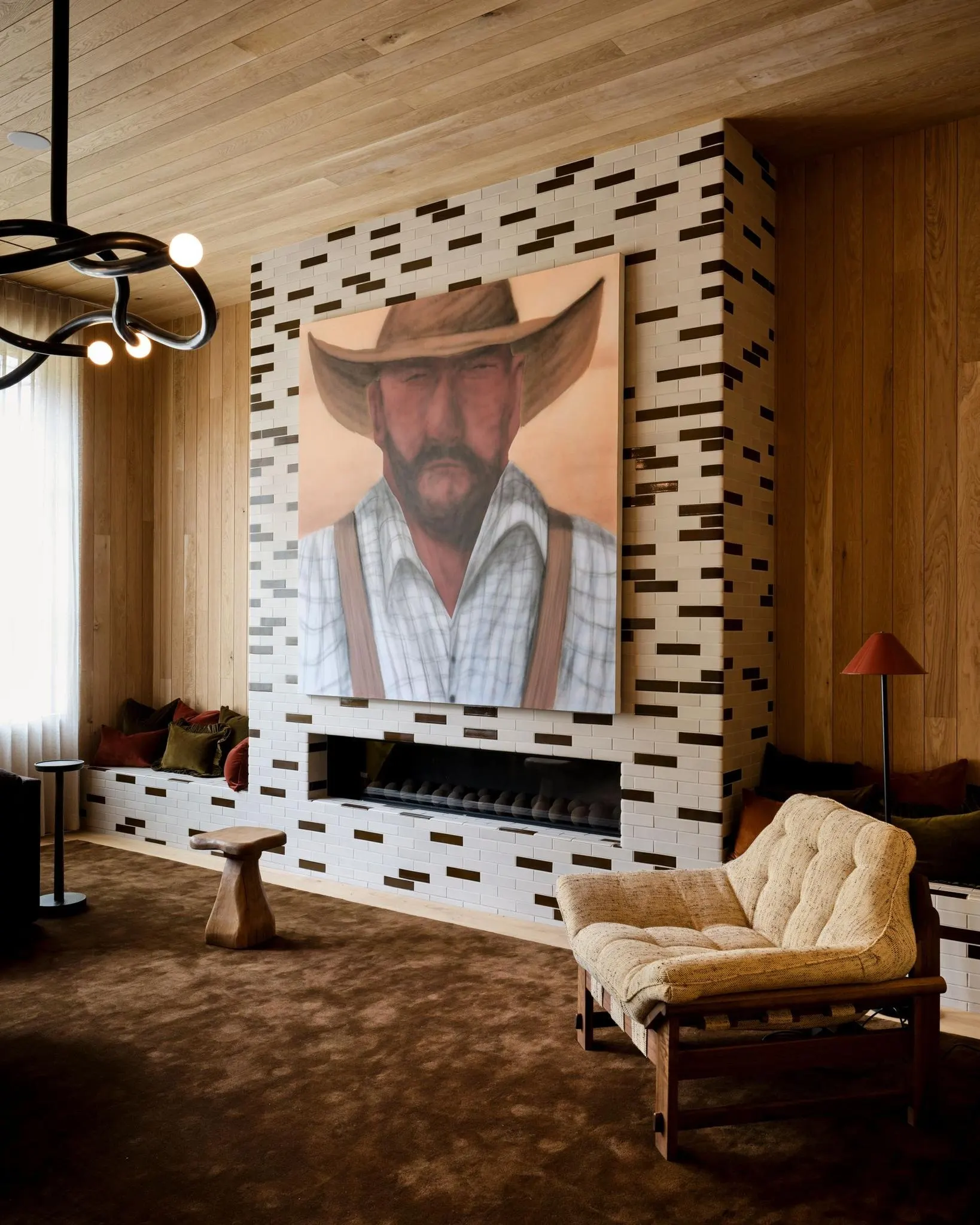 Large painting of a bearded man in a cowboy hat above a brick fireplace, artwork by Martin Kačmarek