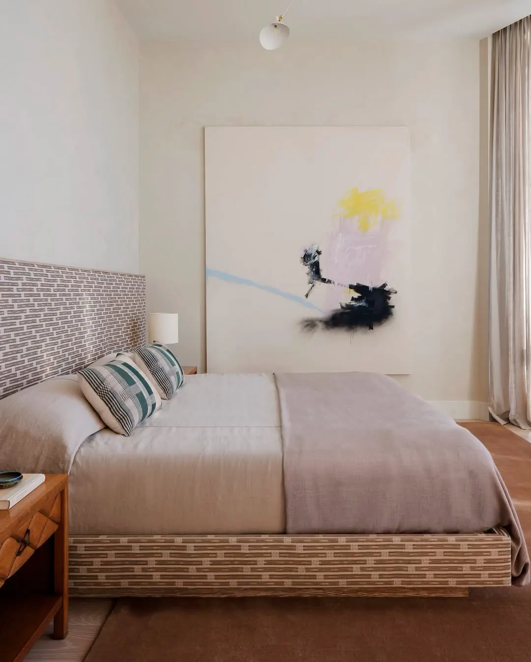 Abstract painting with yellow, pink and black brushstrokes above a bed with a patterned headboard, artwork by Jenny Brosinski