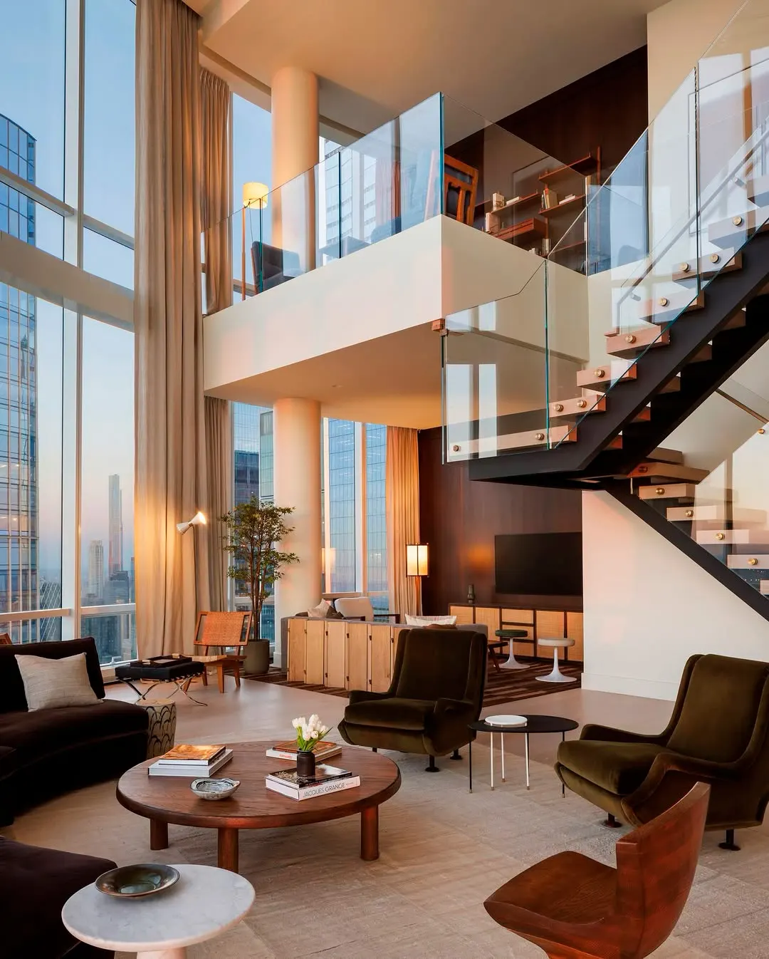 Double-height living room with floor-to-ceiling windows, a floating glass staircase and velvet armchairs in a 15 Hudson Yards penthouse