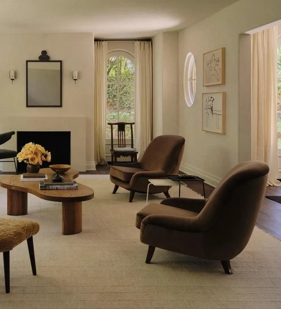 Sitting room with brown velvet armchairs, a kidney-shaped coffee table and two framed line drawings