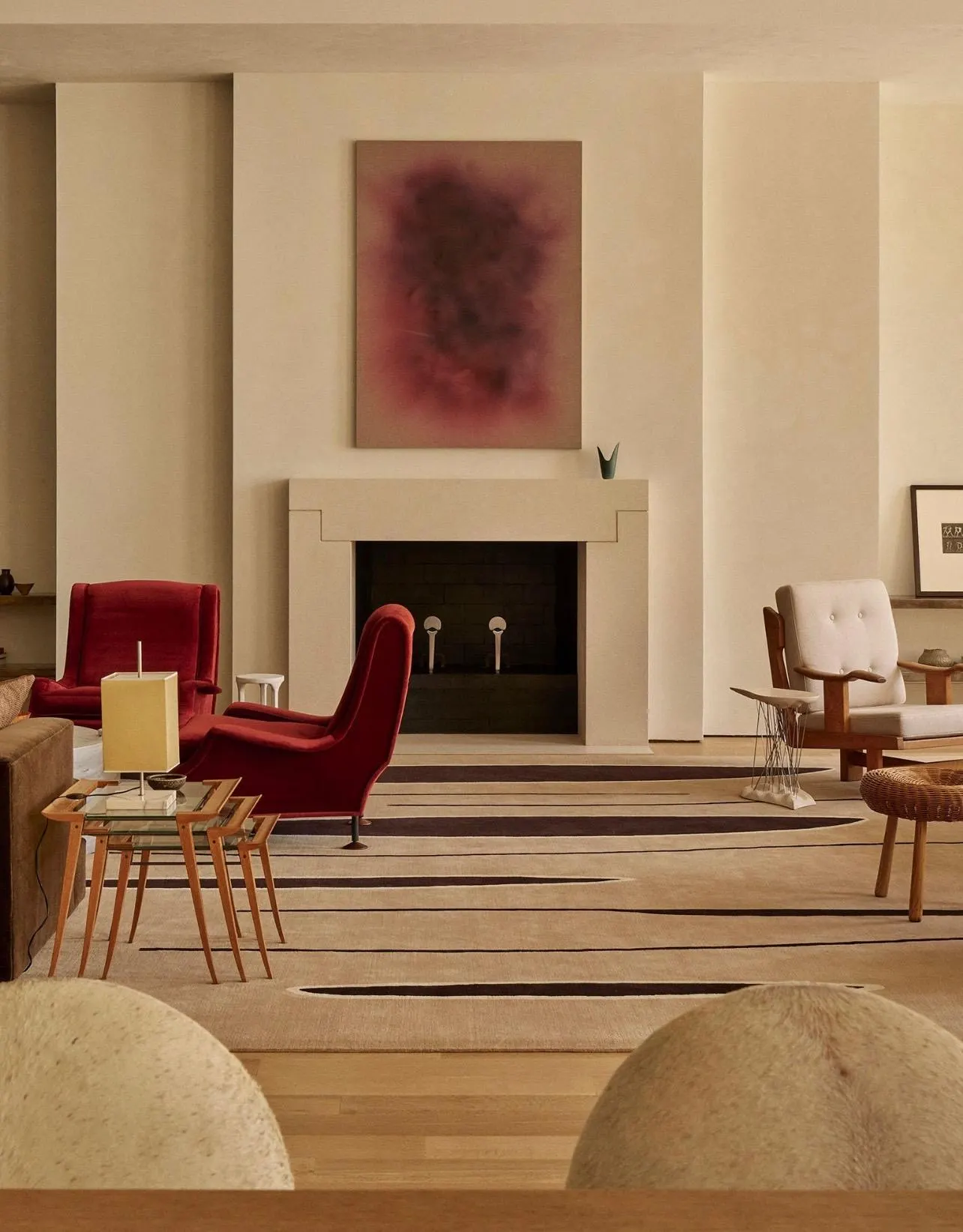 Living room with a stone fireplace beneath a large deep red abstract painting and red velvet armchairs