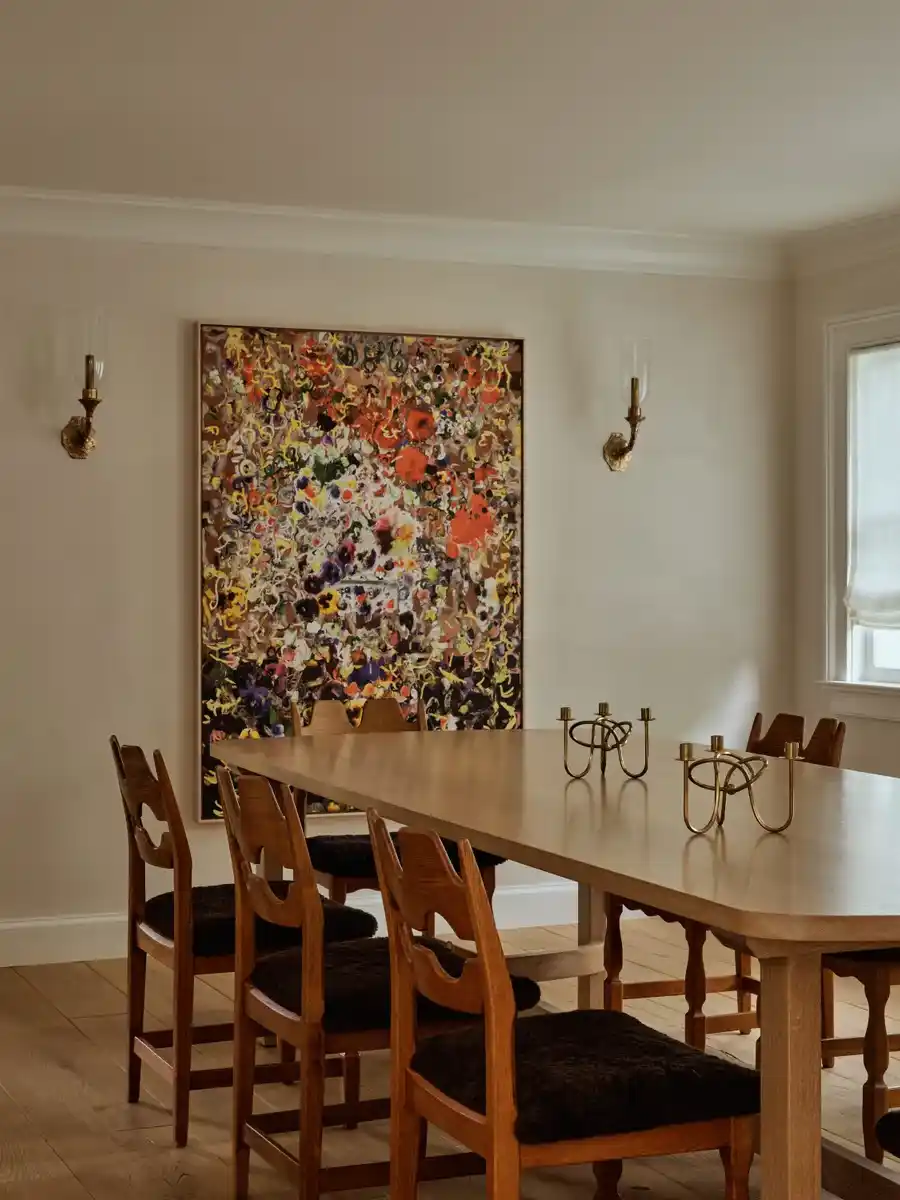 Dining room with a wood table, carved chairs and a large colorful abstract painting of dense flower-like marks