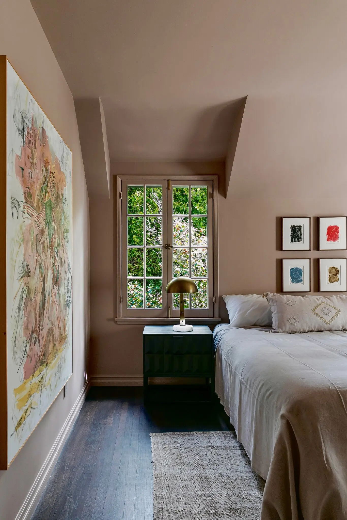 Bedroom with a large pastel abstract painting, a grid of four small framed works and a garden window