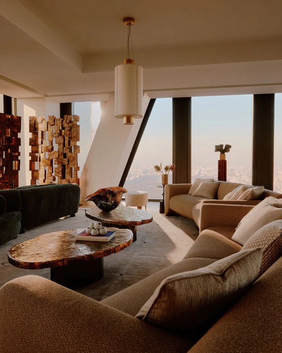 Living room with curved sofas, glossy amber coffee tables and a tall bronze relief sculpture by sunlit windows