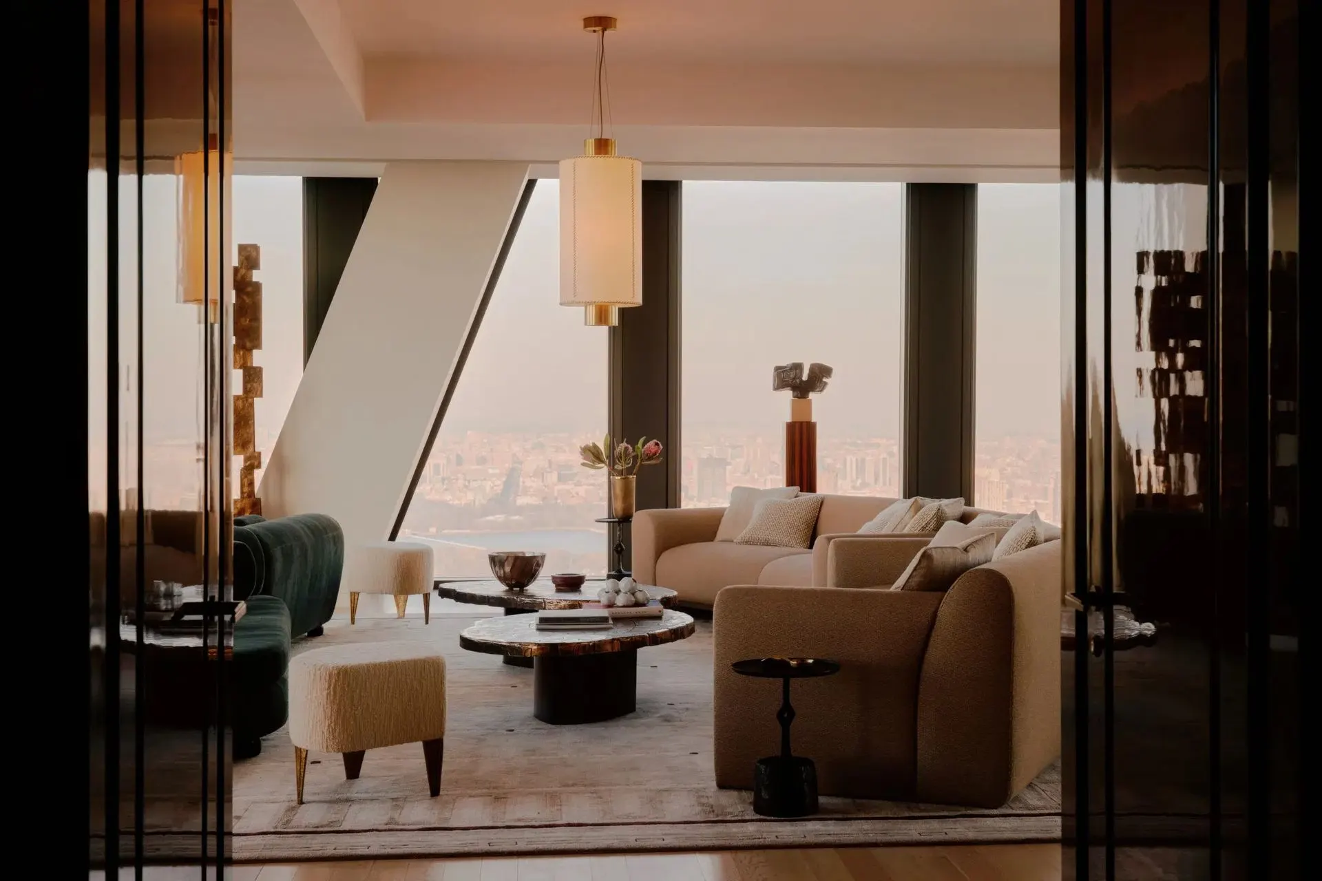 Living room with curved boucle sofas, a pendant lamp and floor-to-ceiling windows above the city at dusk
