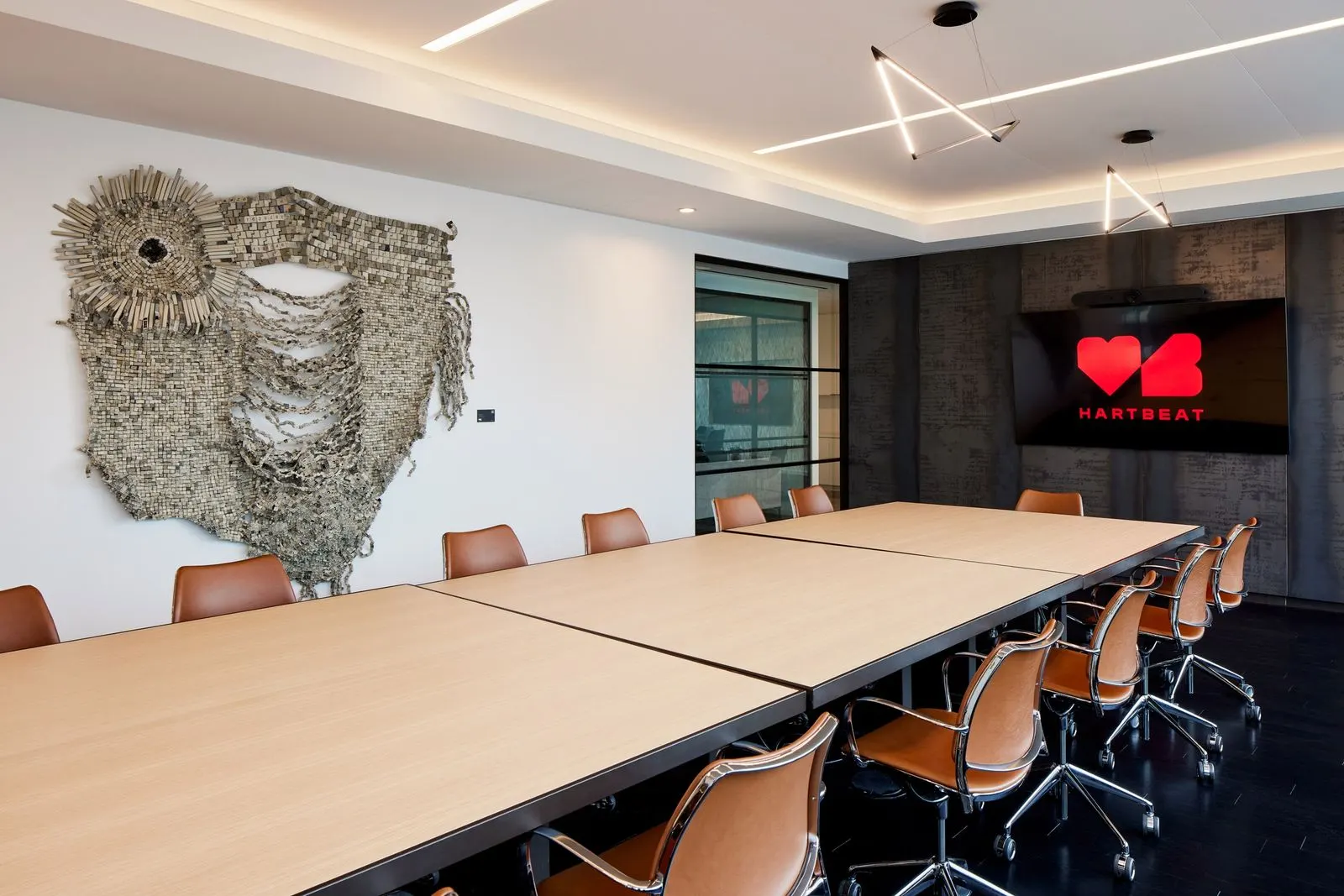 Conference room with a large woven fiber wall sculpture, long wooden tables and tan leather chairs in Kevin Hart's office