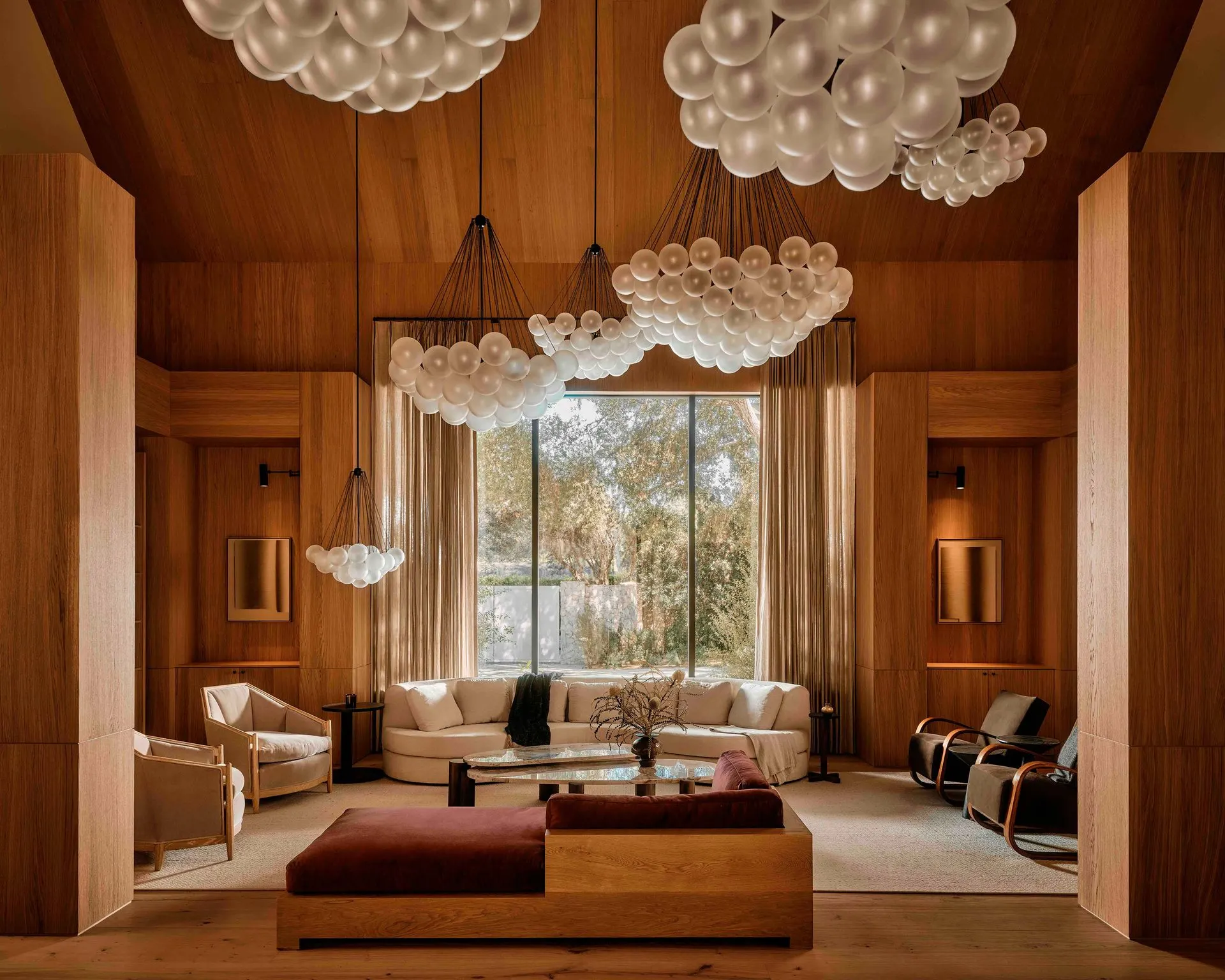 Wood-paneled double-height living room with clusters of glass globe chandeliers and a large picture window