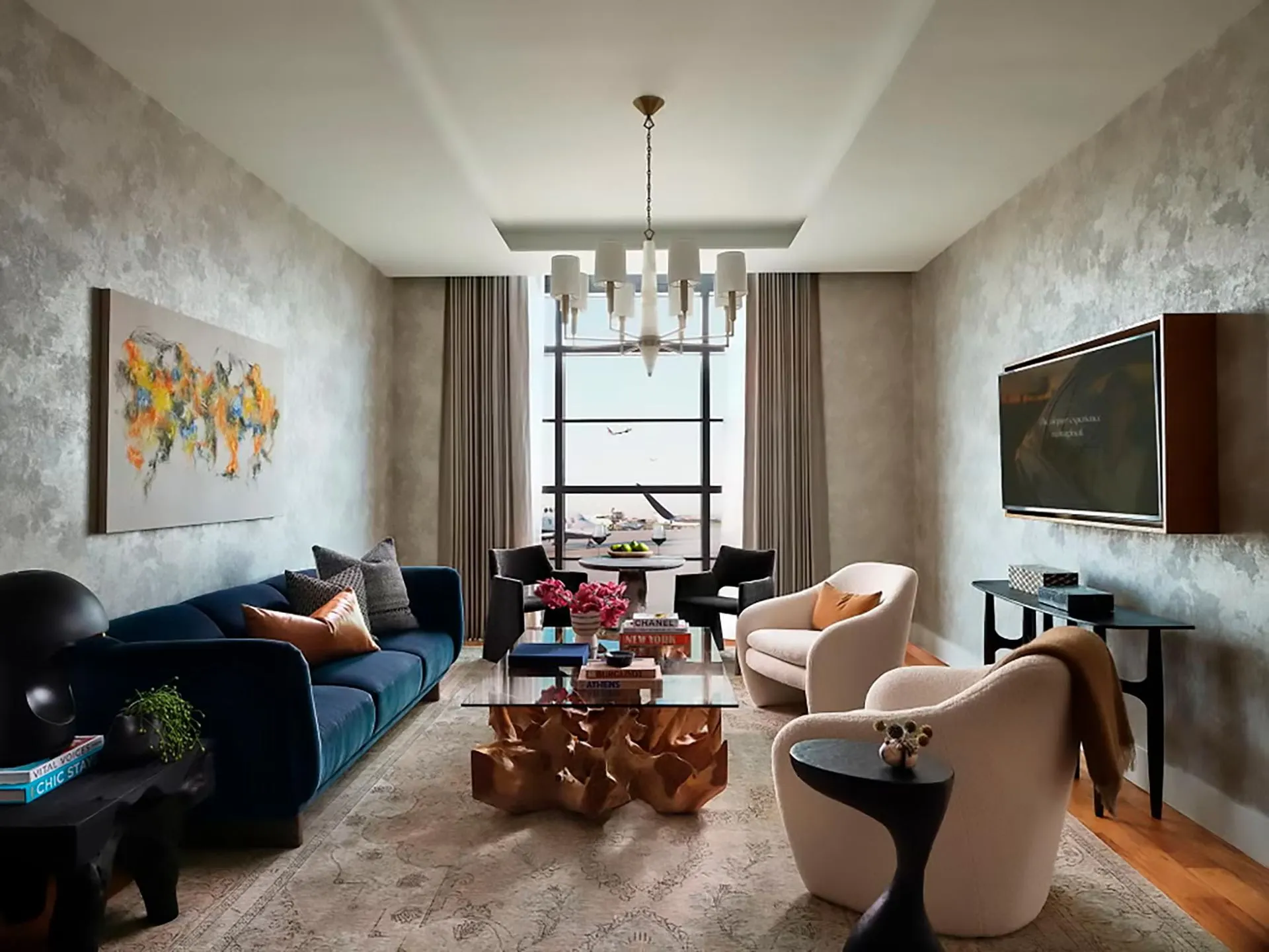 Living room with a navy velvet sofa, cream armchairs and a colorful abstract painting on silvered wallpaper