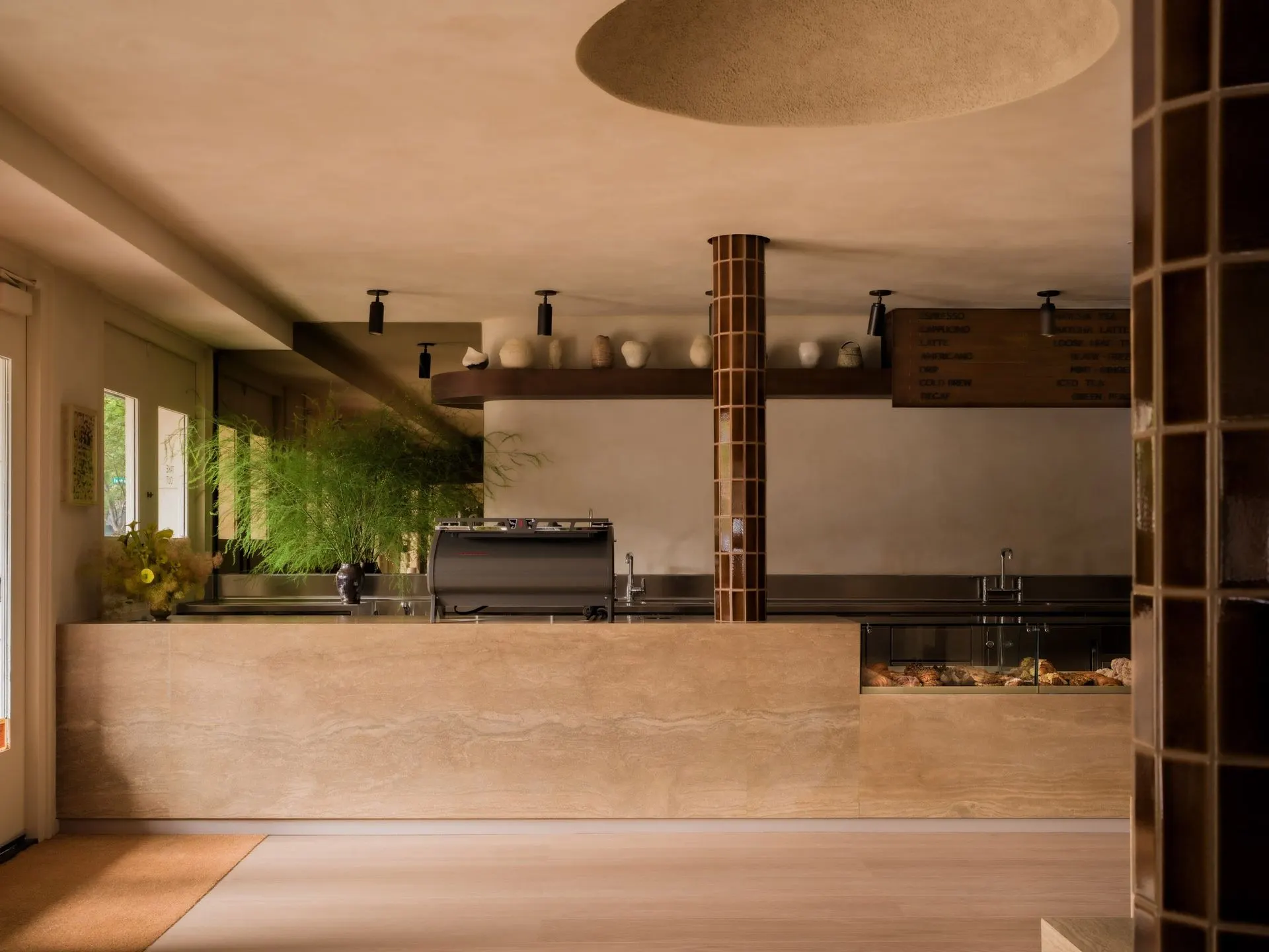 Cafe counter of travertine with a tiled column, espresso machine and pastry case inside the Meadow Lane grocery
