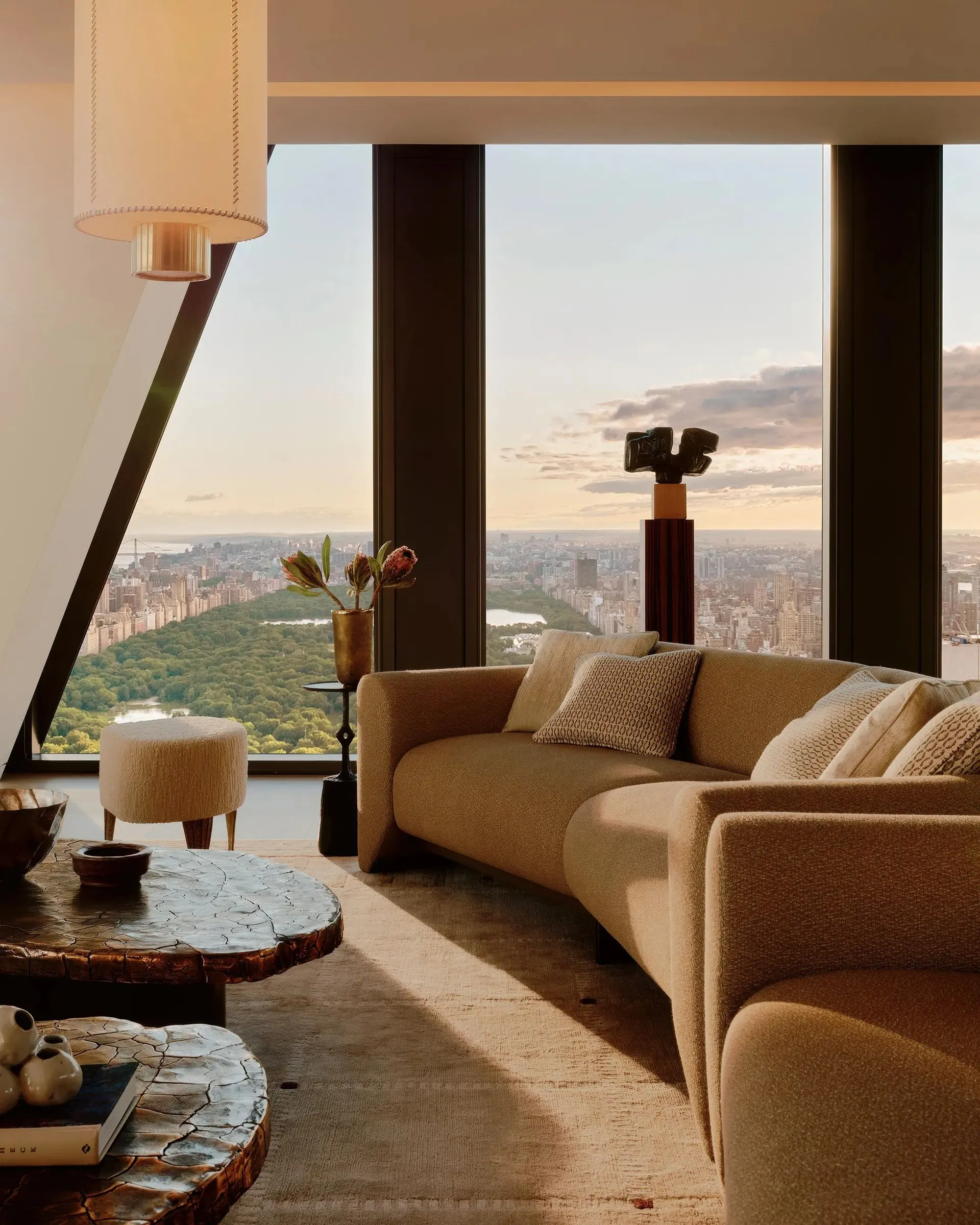 Living room with a curved sofa, a sculpture on a pedestal and tall windows overlooking Central Park