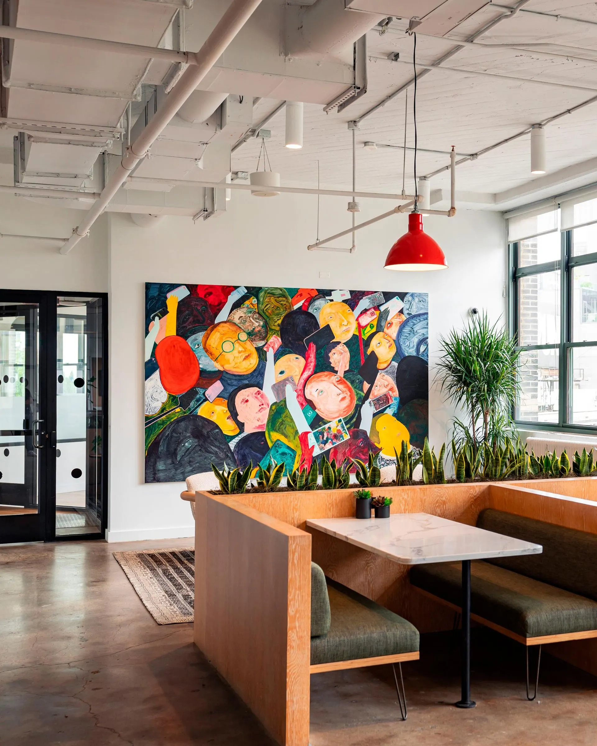 Office cafe with wood booths, a red pendant lamp and a large colorful painting of crowded cartoon faces