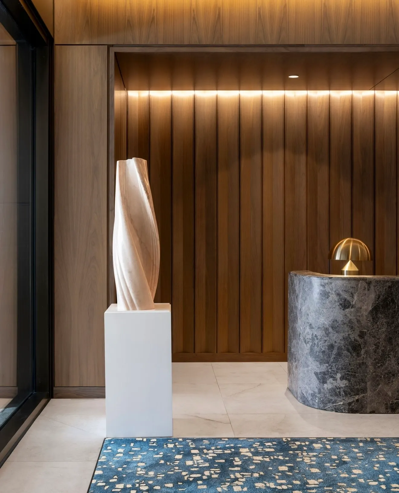 Residential lobby with a carved stone sculpture on a white plinth beside a gray marble reception desk