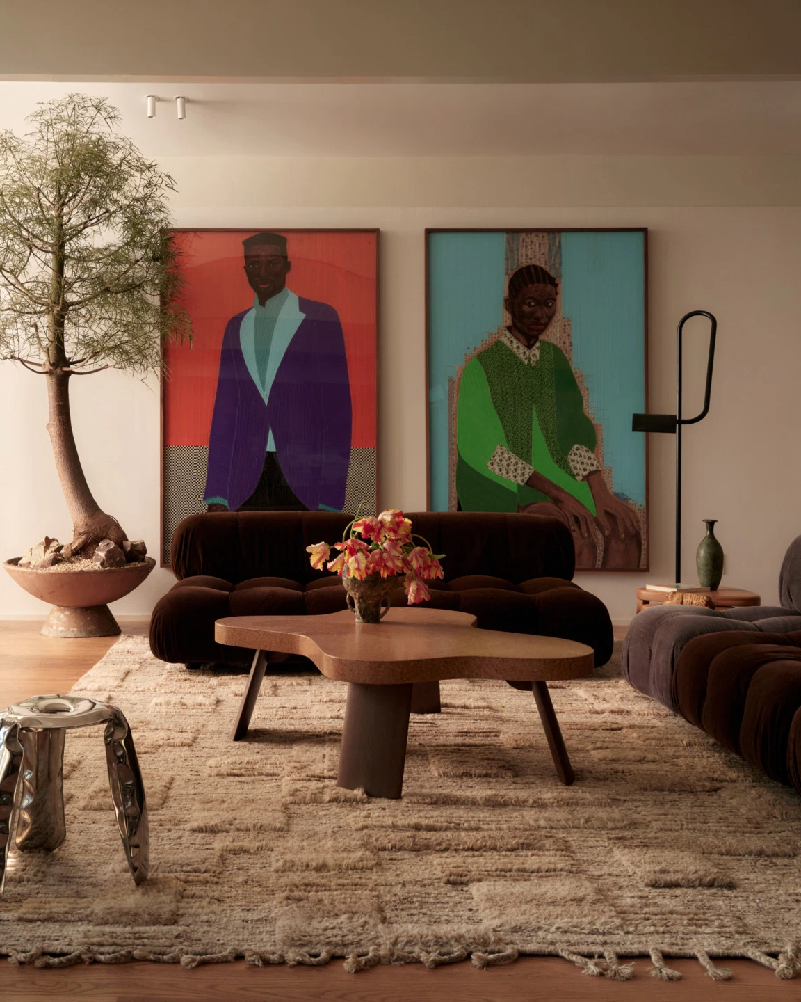 Living room with two large portrait paintings of seated figures above a dark velvet sofa and sculptural coffee table