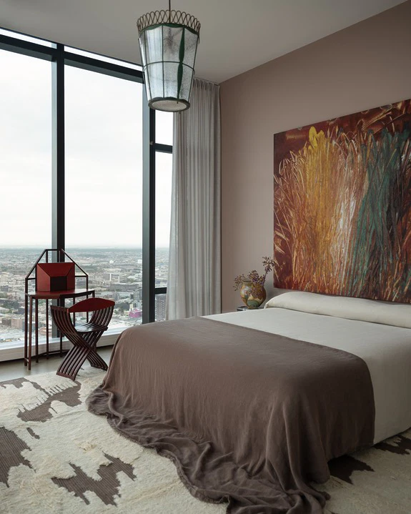 Bedroom with a large abstract painting in red, yellow and green above the bed beside floor-to-ceiling city windows