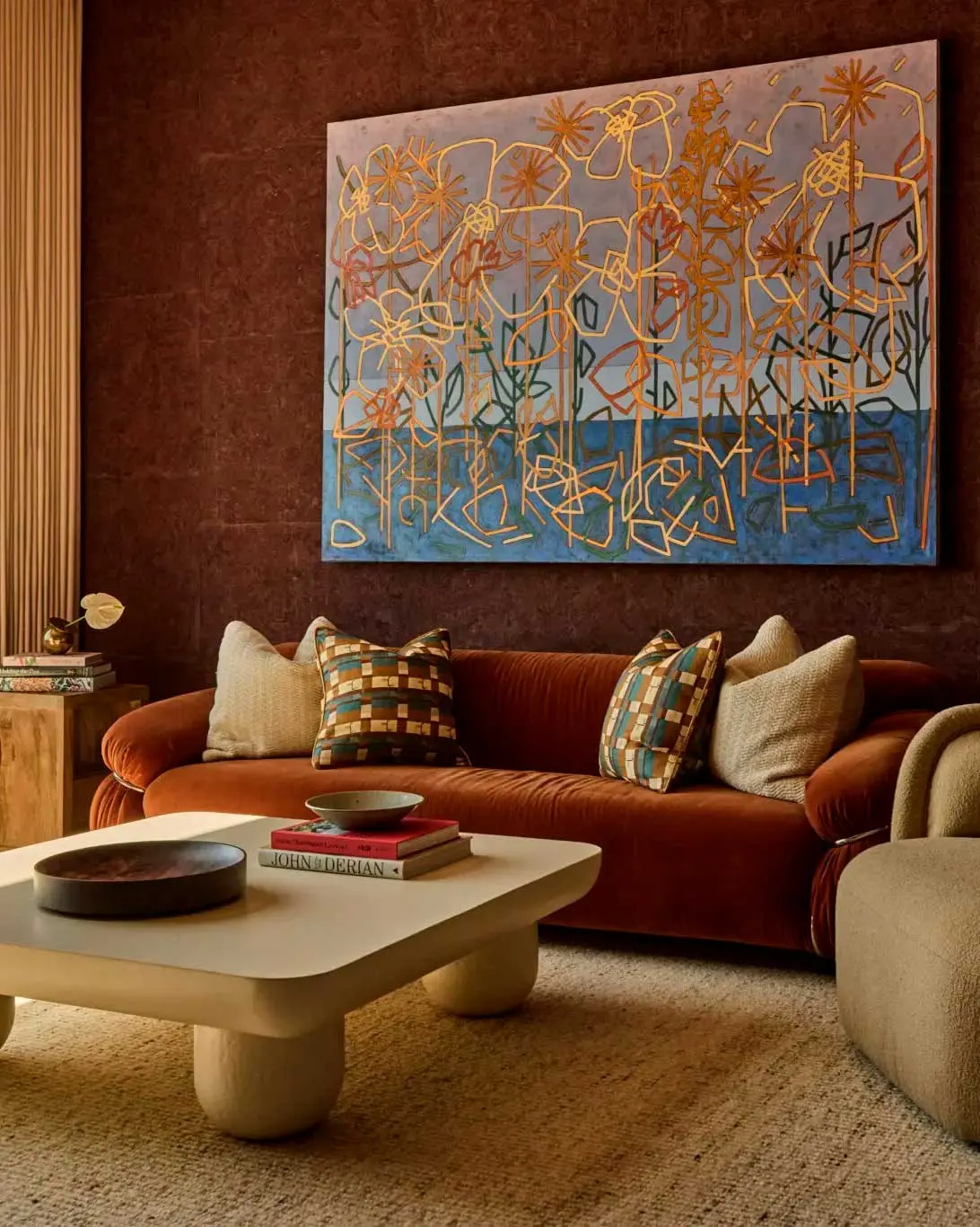 Large abstract floral painting in gold, orange and blue above a rust velvet sofa in the PS DFW terminal lounge