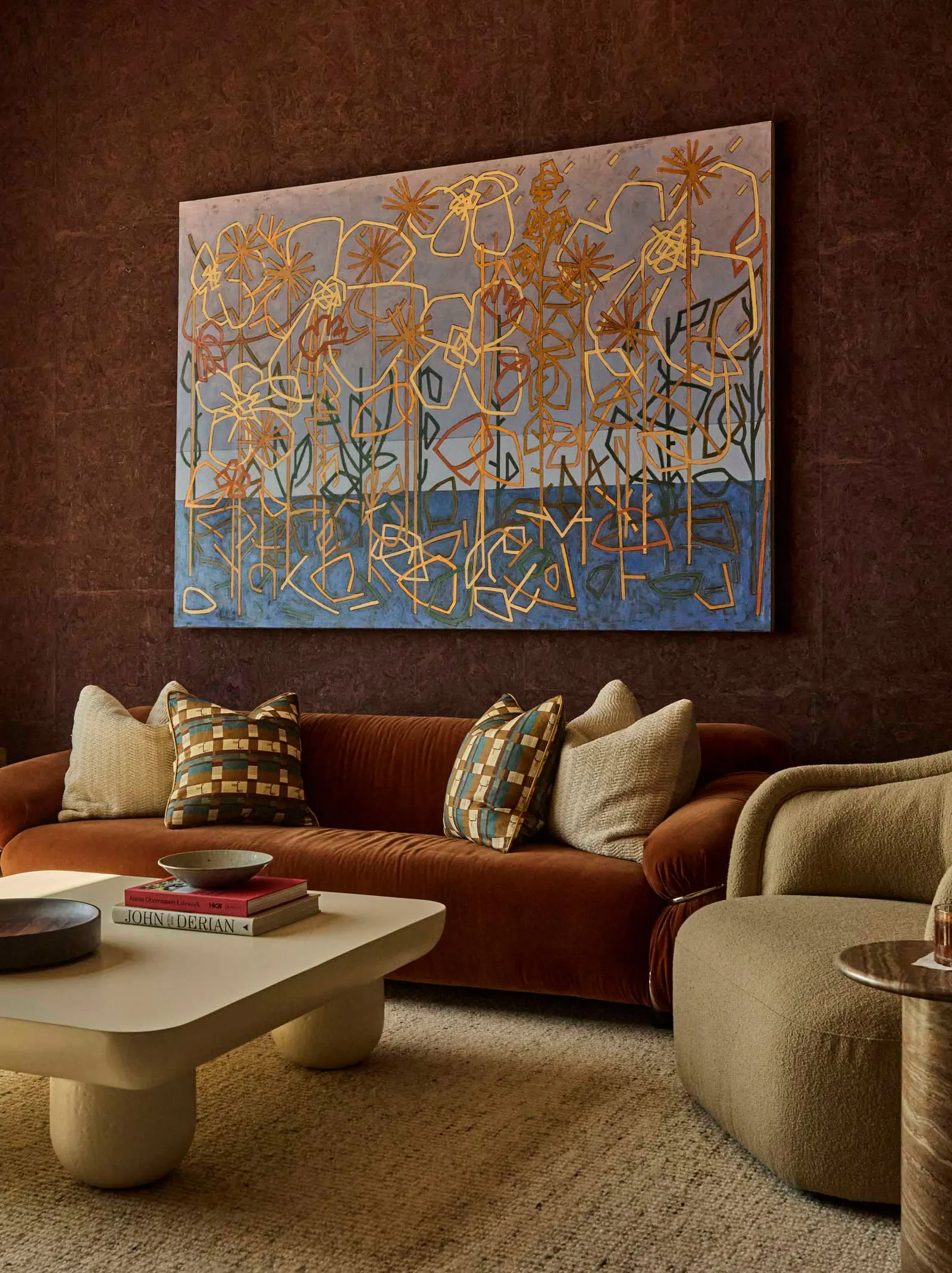 Lounge with a rust velvet sofa beneath a large blue and gold painting of line-drawn flowers